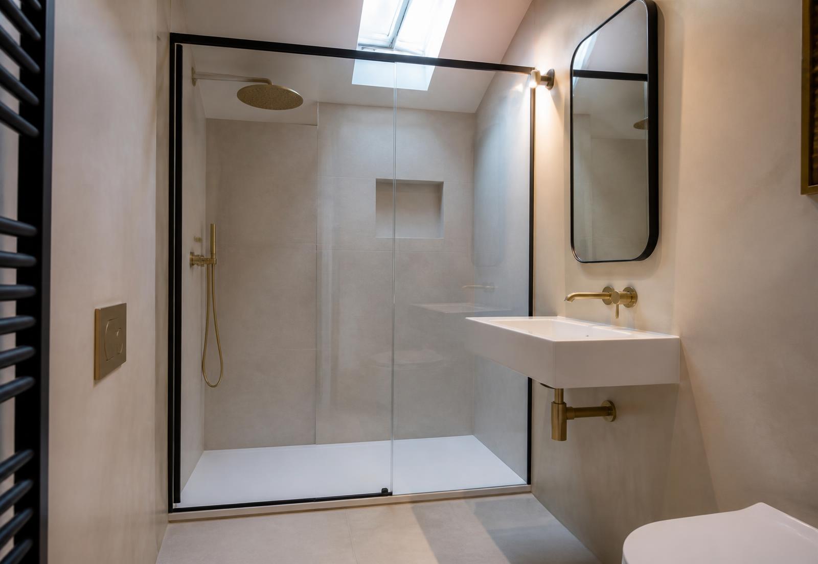Loft ensuite shower room with pale stone tiling, black framed screen and brushed brass fittings